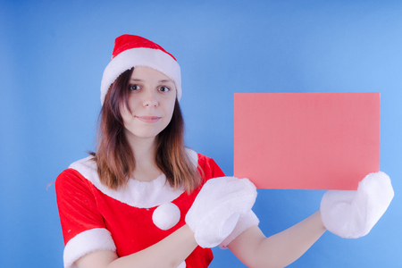Portrait of a young girl dressed as Santa Claus on a blue background. Happy New Year and merry Christmas!の写真素材