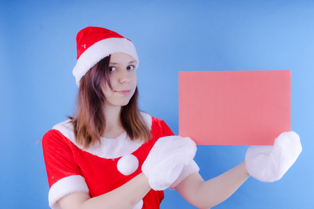 Portrait of a young girl dressed as Santa Claus on a blue background. Happy New Year and merry Christmas!の写真素材