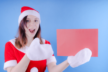 Portrait of a young girl dressed as Santa Claus on a blue background. Happy New Year and merry Christmas!の写真素材