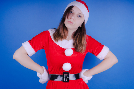Portrait of a young girl dressed as Santa Claus on a blue background. Happy New Year and merry Christmas!の写真素材