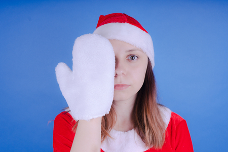 Portrait of a young girl dressed as Santa Claus on a blue background. Happy New Year and merry Christmas!の写真素材