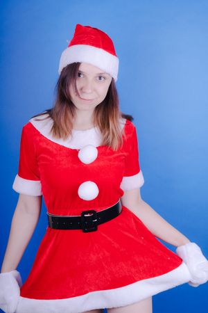 Portrait of a young girl dressed as Santa Claus on a blue background. Happy New Year and merry Christmas!の写真素材