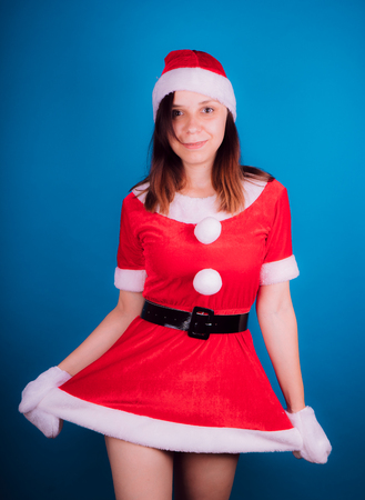 Portrait of a young girl dressed as Santa Claus on a blue background. Happy New Year and merry Christmas!の写真素材