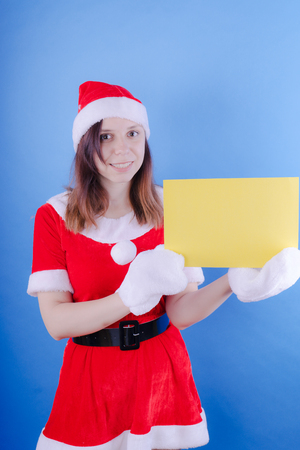 Girl in a suit Santa Claus with a sign on a blue background. The concept of discounts and sales for Christmas. Discount on holiday. Empty space for textの写真素材