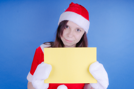 Girl in a suit Santa Claus with a sign on a blue background. The concept of discounts and sales for Christmas. Discount on holiday. Empty space for textの写真素材