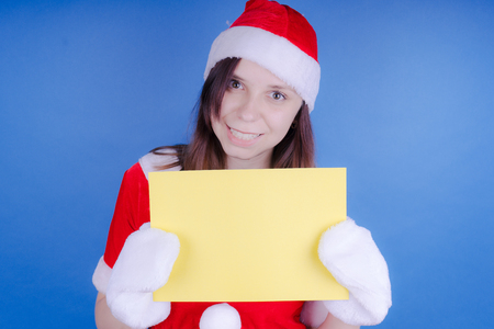 Girl in a suit Santa Claus with a sign on a blue background. The concept of discounts and sales for Christmas. Discount on holiday. Empty space for textの写真素材
