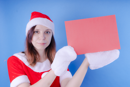 Girl in a suit Santa Claus with a sign on a blue background. The concept of discounts and sales for Christmas. Discount on holiday. Empty space for textの写真素材