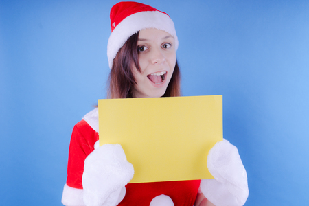 Girl in a suit Santa Claus with a sign on a blue background. The concept of discounts and sales for Christmas. Discount on holiday. Empty space for textの写真素材