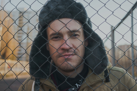 Happy handsome young man in cap with earflaps. The young man in the fur hat. standing on a cloudy day. emotional portrait of a student. street styleの写真素材