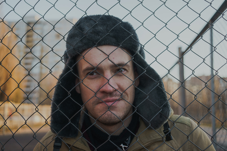 Happy handsome young man in cap with earflaps. The young man in the fur hat. standing on a cloudy day. emotional portrait of a student. street styleの写真素材