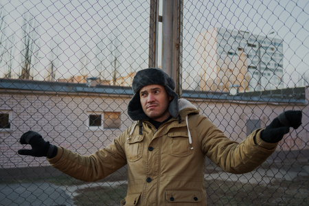Happy handsome young man in cap with earflaps. The young man in the fur hat. standing on a cloudy day. emotional portrait of a student. street styleの写真素材