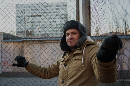 Happy handsome young man in cap with earflaps. The young man in the fur hat. standing on a cloudy day. emotional portrait of a student. street styleの写真素材