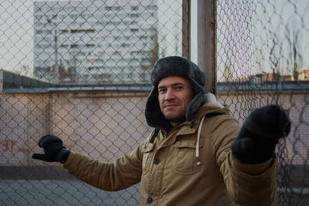 Happy handsome young man in cap with earflaps. The young man in the fur hat. standing on a cloudy day. emotional portrait of a student. street styleの写真素材