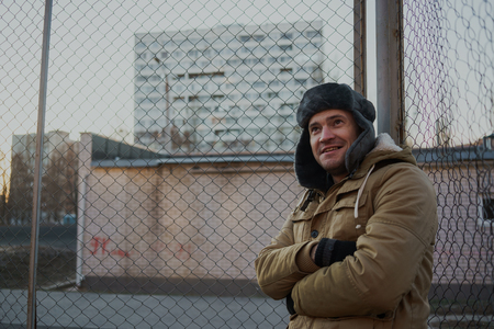 Happy handsome young man in cap with earflaps. The young man in the fur hat. standing on a cloudy day. emotional portrait of a student. street styleの写真素材