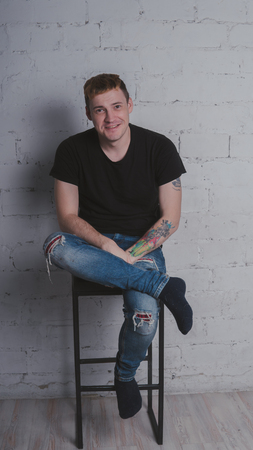 A handsome man in black t-shirt, against a gray brick wall. Brutal guy with a tattooの写真素材