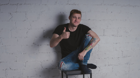 A handsome man in black t-shirt, against a gray brick wall. Brutal guy with a tattooの写真素材