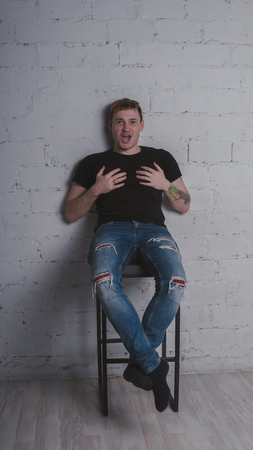 A handsome man in black t-shirt, against a gray brick wall. Brutal guy with a tattooの写真素材