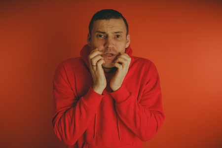 Crazy and charismatic guy posing on orange background. A man in a red tracksuit.