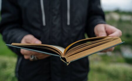 Man reading book in green hilly field