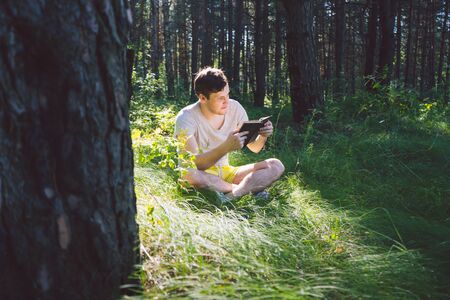 Man reading a book in a green summer forest.の写真素材