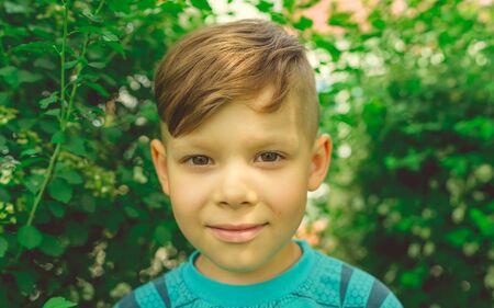Serious boy in bright green garden. Adorable cute kid with stylish hair dress standing in bright...