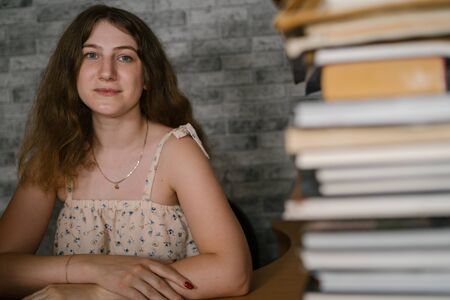 Tired female student reading among books. Pensive young woman sitting at table with pile of book and...