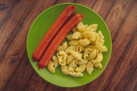 pasta and sausages in a green plate on a wooden table. pasta in closeupの写真素材