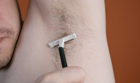 Attractive man with a blue razor in his hands is going to shave hair with armpits isolatedの写真素材
