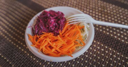 Salads from fresh vegetables: cabbage, carrots, beets in a white plastic plate on the table.の写真素材