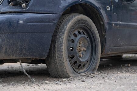 Old car with deflated wheel parked on streetの写真素材