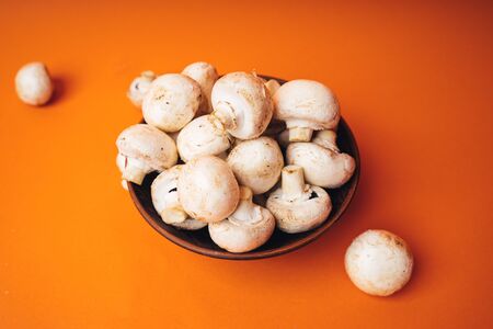 Mushrooms in a wooden bowl on an orange background. The small white mushrooms in a plate and scattered near itの写真素材