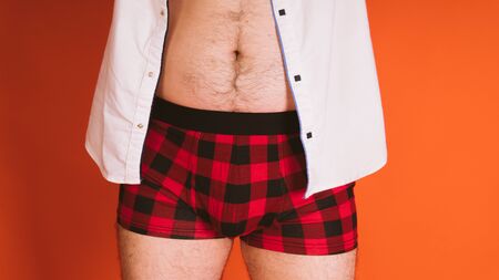 Male naked body in the plaid boxers and in white shirt unbuttoned on orange background.の写真素材