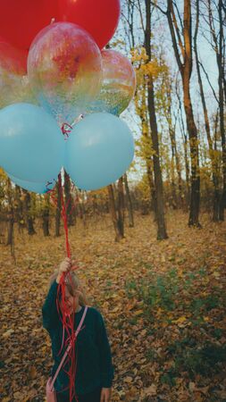 A little girl are holding balloons on walk in autumn forestの写真素材