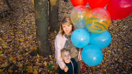 A beautiful young mother hugs her a little adorable daughter and holds the colorful balloons on a...