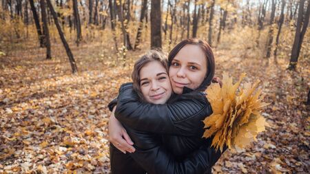 Two young women are hugging on a walk in the autumn forest. Girlfriends met to walk in a warm weather.の写真素材
