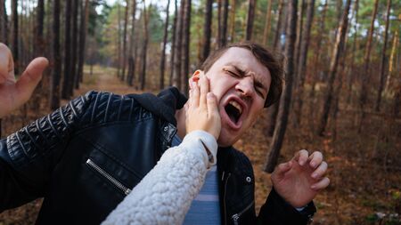 A womans hand hits a mans face in the autumn forest. An emotional male is getting slapped in face, while shouting with closed eyes in a fear.の写真素材