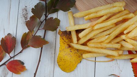 The appetizing french fries are on a wooden board with decoration of autumn leaves