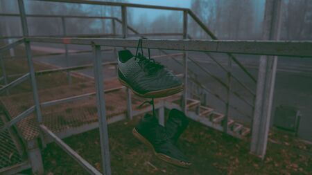 An old shoes are hanging by the laces on a fence