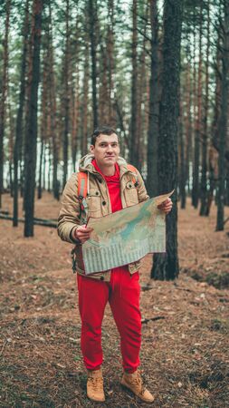 A traveling man with map in woods. A portrait of the handsome man with a backpack, standing near a...