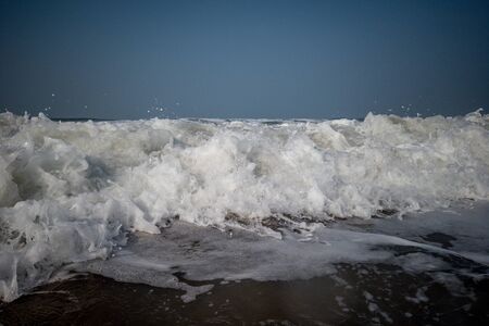 The low tide from the sandy beach. Ocean waves are splashing on the shore