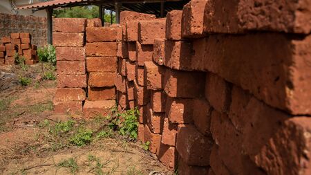Shabby red bricks stacked on sandy ground with grass on sunny day in yard