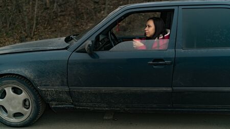 Long haired woman with disposal cup at front seat of car looking at window