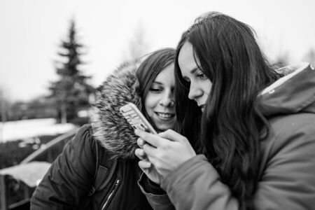 Two women look in mobile phone, considering their photos on walk. Black and white photo.の写真素材