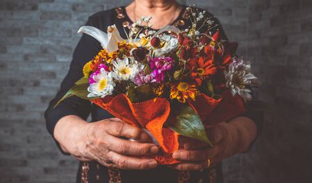 Unrecognizable senior lady carrying wrapped bouquet of colorful flowers during holiday celebration