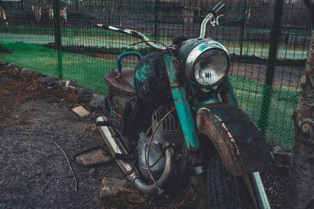 Old rusty motorcycle near fence on ground. Close up of abandoned broken motorbikeの写真素材