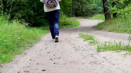 Back view of young female with ornamental backpack walking along path in quiet autumn parkの写真素材