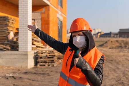 Young woman in hard hat and orange vest showing gesture of approval.