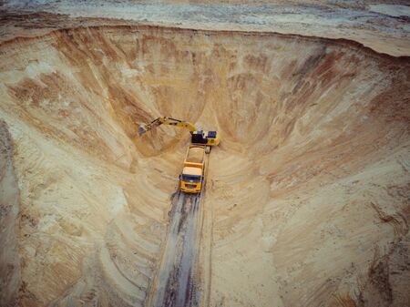 A heavy machinery - excavator and truck are working in the sand quarry.