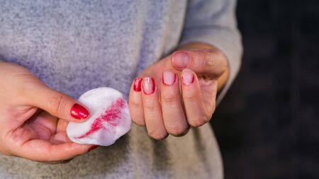 Woman hand removing red nail polish with white cotton pad.