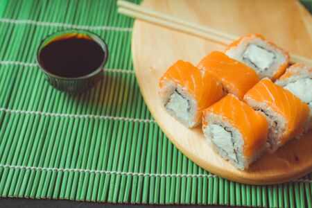 Delicious rolls on wooden board on decorative bamboo napkin. Close up of tasty sushi rolls with chopsticks on cutting boardの写真素材